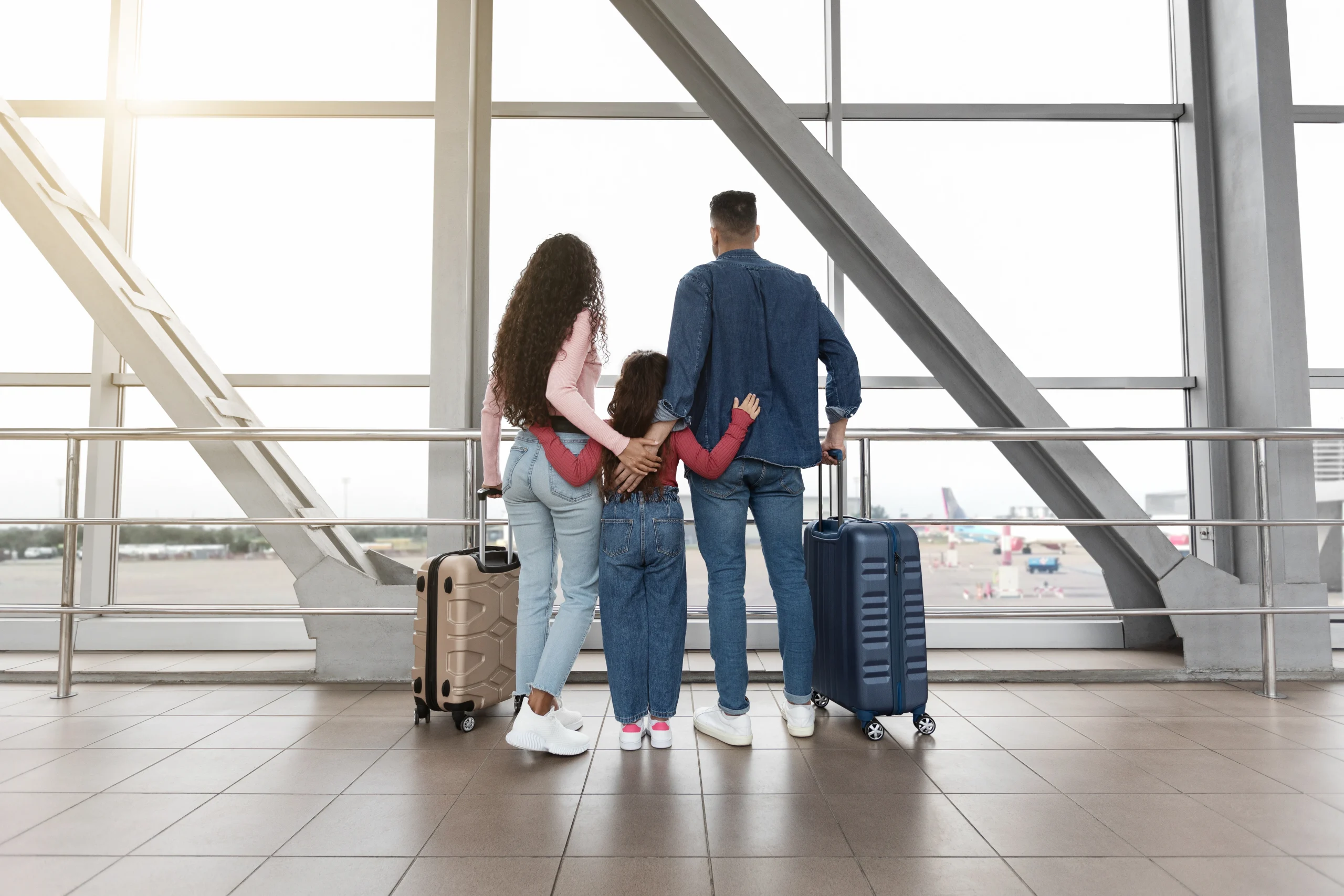 family-with-suitcases-looking-out-window-airport-while-waiting-flight