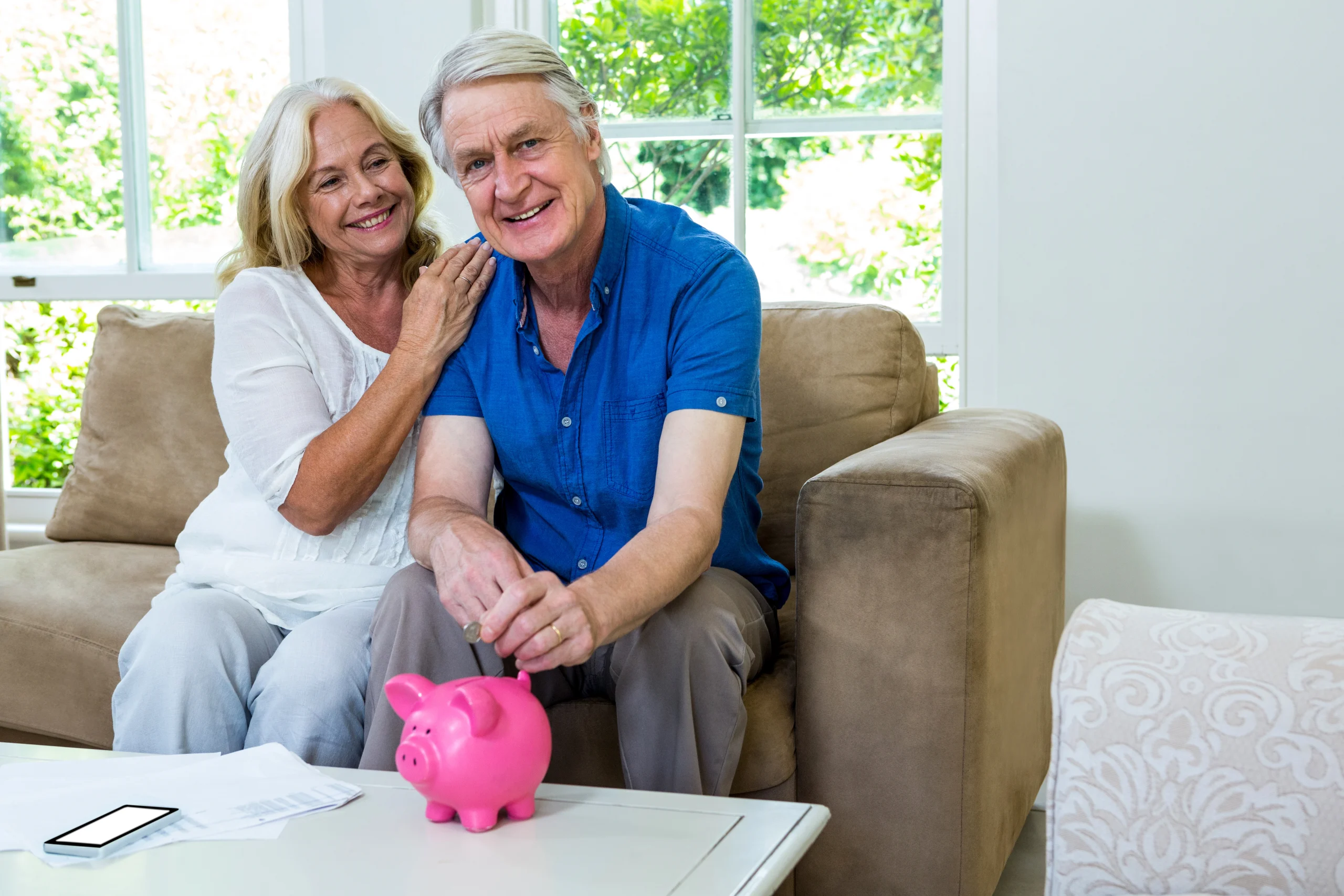 smiling-senior-couple-putting-coin-piggy-bank-home